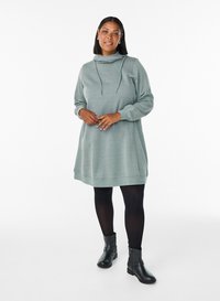 Hoodieklänning med långa ärmar i mjukt, texturerat grått tyg. Har en avslappnad passform, sidofickor och kombineras med svarta ankelboots.