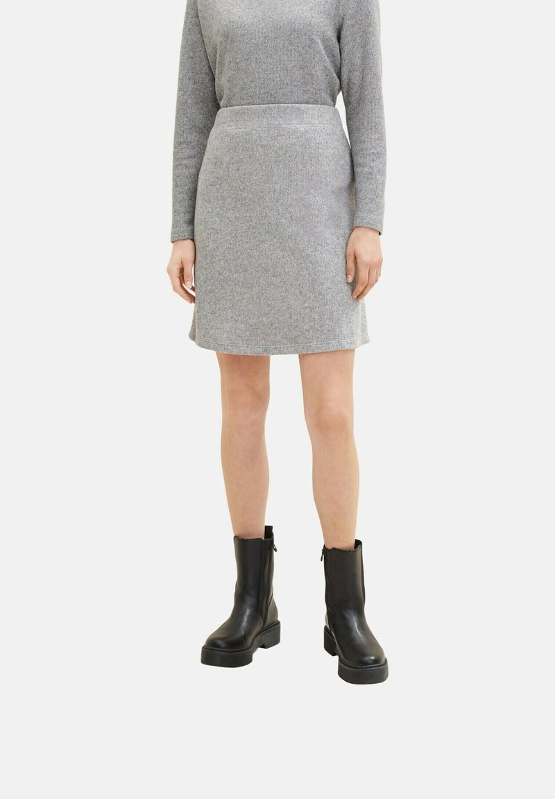 Femme vêtue d'une jupe en maille grise et d'un haut à manches longues assorti, associée à des bottines noires, sur un fond uni.