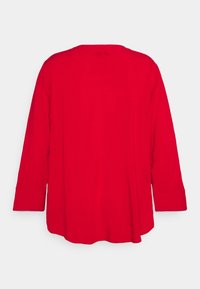 Red long-sleeve shirt with a loose fit, rounded neckline, and finished cuffs. Smooth fabric texture, no visible patterns or hardware.