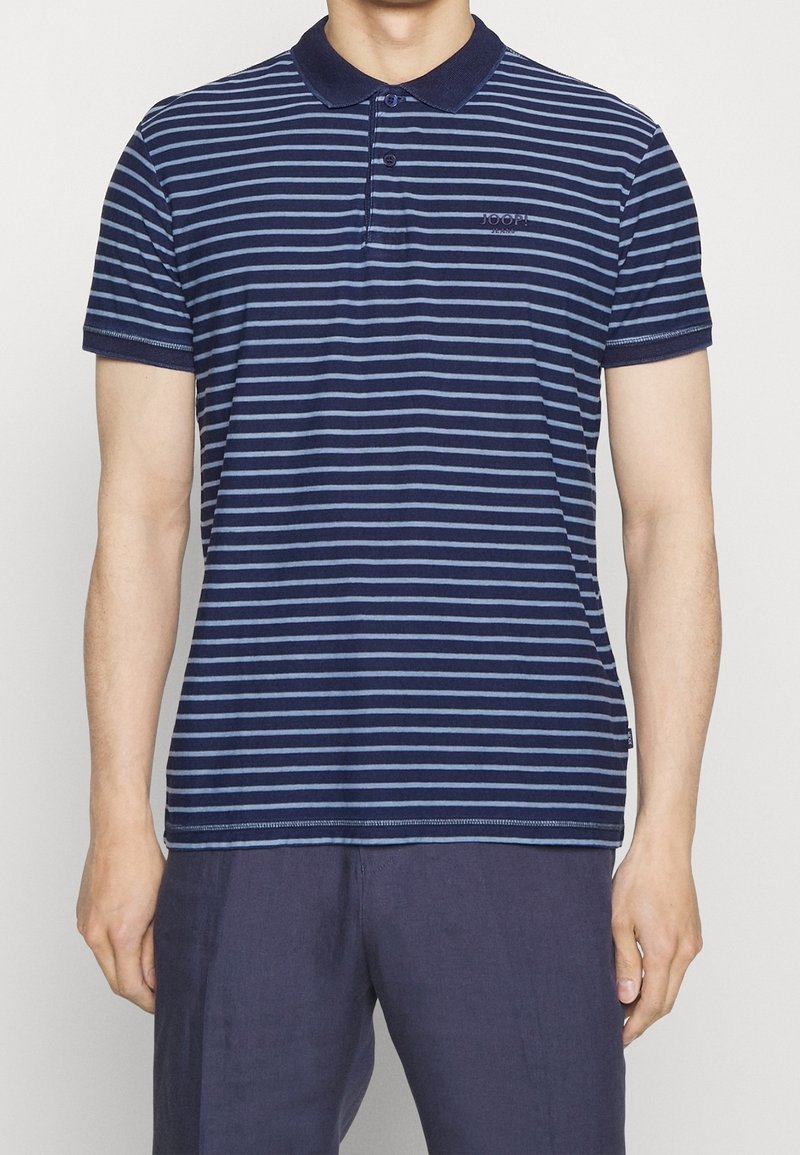 Homme portant un polo à manches courtes rayé horizontalement bleu marine et bleu clair, avec un col et des boutons bleu foncé, associé à un pantalon bleu foncé.