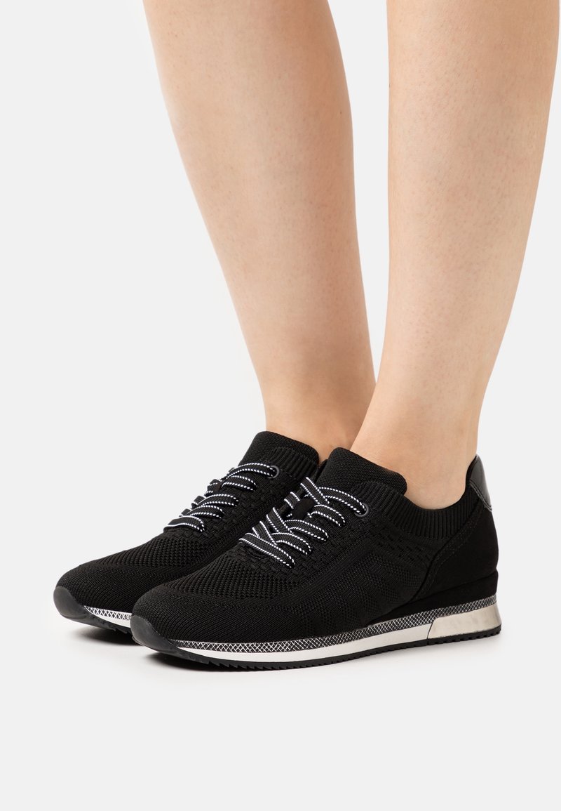 Sneakers in maglia nera con lacci bianchi, una parte superiore testurizzata e un elegante accento argentato sul tallone. Presentano una punta rotonda e una suola imbottita.