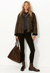 Veste bomber à imprimé léopard en marron foncé avec des manches à revers, portée sur un haut rayé, associée à des leggings noirs et un sac en bandoulière marron.
