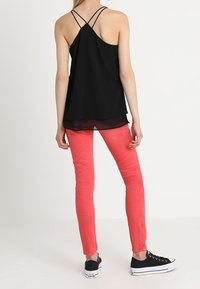 Svart ärmlös topp med korsettsnören, i kombination med korallfärgade tajta jeans och svarta sneakers, som visar en avslappnad outfit.