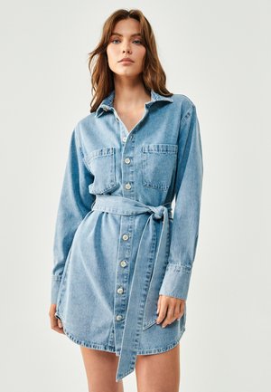 Lichtblauwe denimjurk met lange mouwen, knoopsluiting, twee borstzakken en een bijpassende riem, met een afgeronde zoom en een relaxte pasvorm.