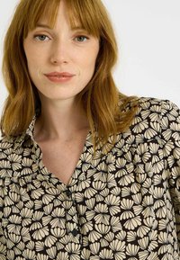 Blusa negra con un estampado floral en crema, con cierre de botones y cuello. Tela suave con un ajuste relajado y textura delicada.