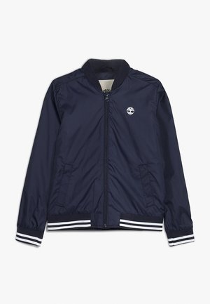 Granatowa kurtka bomberka z zamkiem z przodu, ściągaczem na kołnierzu i mankietach, kieszeniami bocznymi oraz białym logo na lewej piersi. Białe paski na mankietach.