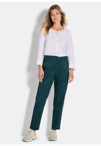 Witte blouse met lange mouwen, een ronde halslijn en een sleutelgatdetail, gecombineerd met donkergroene, taps toelopende broeken van zachte stof en lichte sneakers.