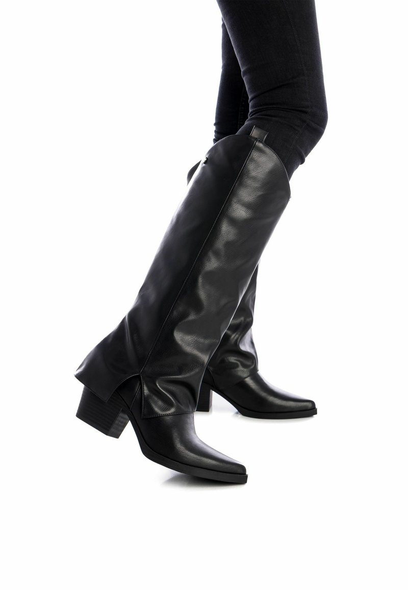 Botas de cuero negras hasta el muslo con punta afilada y tacón grueso. Presentan una textura suave y elegante, además de aberturas laterales para un detalle adicional.