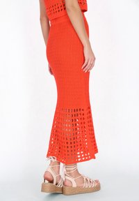 Geweven oranje maxi rok met een aansluitende top en een uitlopende onderkant met open ruitpatroon details. Gekoppeld met beige gespsandalen met een sleehak.