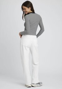 Haut à manches longues noir et blanc à rayures associé à un pantalon blanc taille haute. Tenue complétée par des baskets gris clair. Design simple.