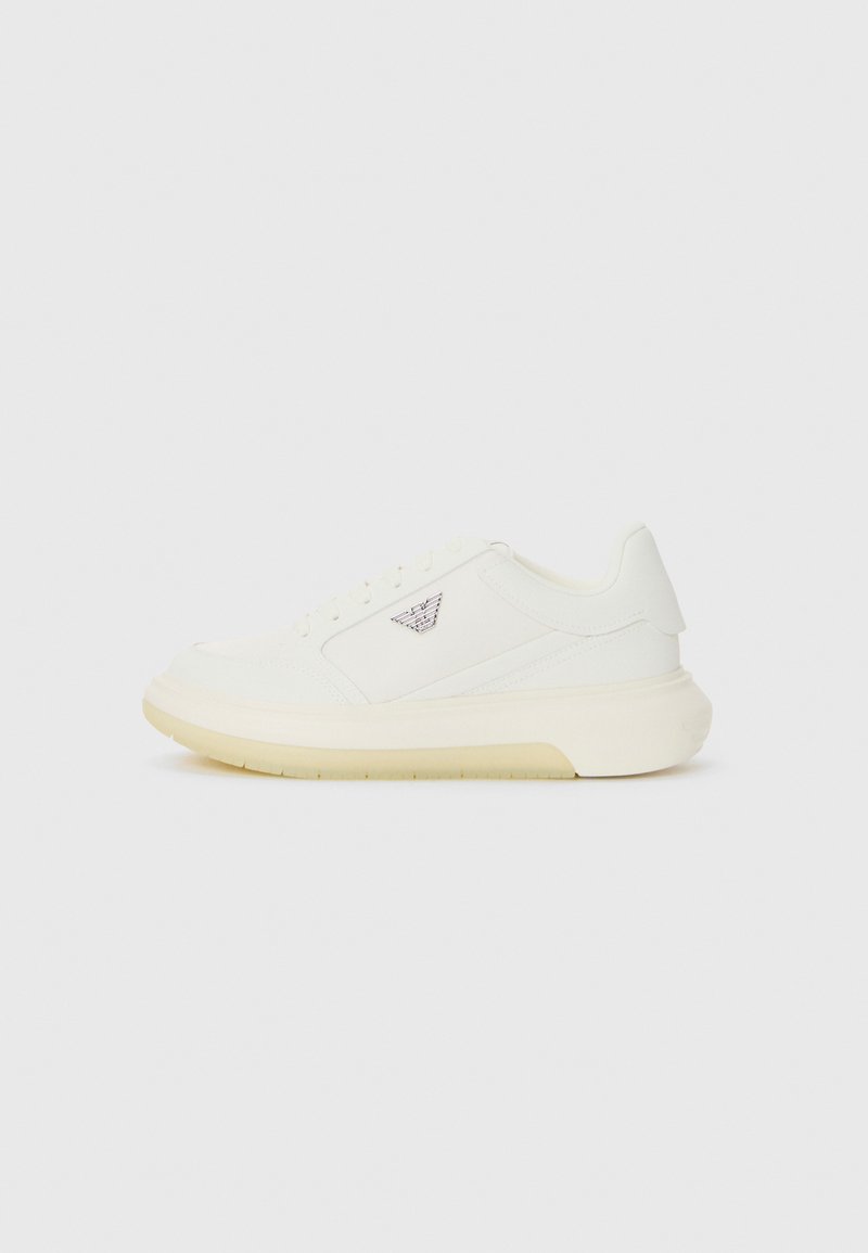 White sneaker with a smooth leather upper, light beige sole, and tonal stitching. Features a logo on the outer side and five eyelets for laces.