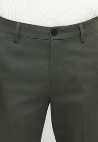 Dark green trousers made of smooth fabric, featuring a zip fly, button closure, and front pockets with a classic cut.