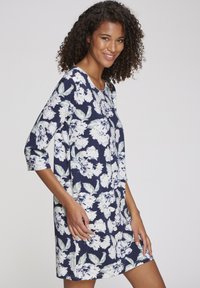 Abito a stampa floreale con sfondo blu navy, fiori bianchi e foglie verdi, scollo rotondo e maniche a tre quarti.