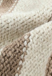 Nahaufnahme eines dicken, strukturierten gestrickten Stoffes mit abwechselnd beigem und hellbraunem Garn in einem gewebten Muster.