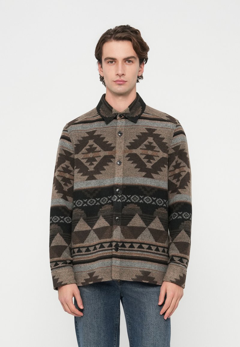 Chaqueta camisa de lana con un patrón geométrico en tonos marrón, negro y gris, cierre frontal con botones y cuello negro.