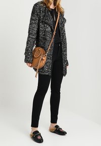 Czarny i biały, teksturowany długi kardigan, czarna bluzka, dopasowane czarne spodnie, brązowa, okrągła torba na ramię, czarne mokasyny z futerkiem i kwiatowym detalem.