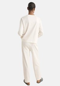 Ensemble de vêtements d'intérieur couleur crème comprenant un haut à manches longues et un pantalon assorti, avec une coupe décontractée et une texture douce. Design à faible contraste.