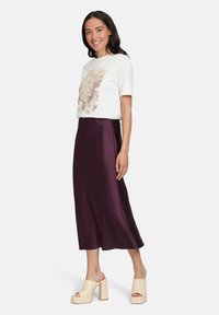 T-shirt bianco con design floreale, abbinato a una gonna in satin viola profondo e fluente, e sandali con tacco a blocco color crema.