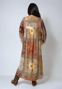 Robe longue à motifs avec des manches bouffantes dans des tons chauds de doré, marron et orange. Présente des motifs floraux complexes et une silhouette fluide.