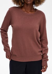 Brązowy sweter dzianinowy z okrągłym dekoltem, długim rękawem i ribbém u dołu. Posiada małą metkę z logo w dolnym lewym rogu. Miękka faktura.