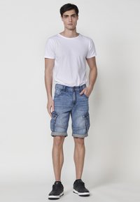 Lichte blauwe denim cargoshorts met opgerolde manchetten, zijzakken en een casual pasvorm. Gecombineerd met een eenvoudige witte t-shirt met ronde hals.