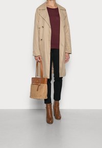 Beige trenchcoat päälle punaviininvärinen neule, mustat housut ja ruskeat nilkkurit. Ruskea nahka- ja kudontakassi, jossa on hihna ja vetskariyksitys.