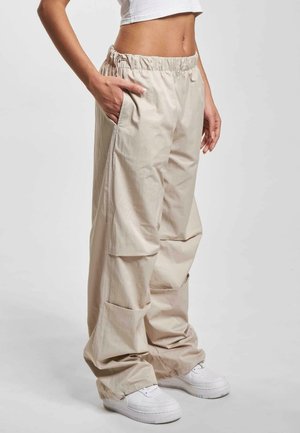 Beige brede bukser med elastisk talje, sidelommer og en glat tekstur, parret med hvide sneakers.