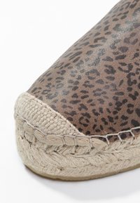 Espadrille imprimée léopard avec une semelle en jute tressé et un contour en tissu beige. Présente une pointe arrondie et une finition texturée sur le dessus.