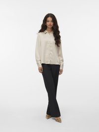 Lichtbeige blouse met lange mouwen, kraag en knopen aan de voorkant, gecombineerd met zwarte rechttoe rechtaan broeken en puntige slangenprint hakken.