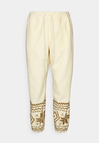 Gräddfärgade sweatpants gjorda av mjukt tyg, med ett brunt geometriskt mönster vid mudden och en elastisk midja med snörning.