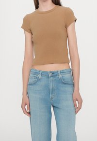 Hnědý žebrovaný krátký top s krátkými rukávy ve stylu crop, spárovaný s světle modrými džínami klasického střihu s pěti kapsami a zapínáním na knoflíky.