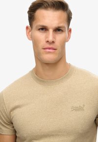 Beige kortemouw t-shirt gemaakt van een textuurstof, met een ronde hals en borduursel op de borst.