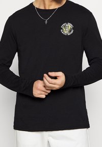 Zwarte lange mouwen t-shirt gemaakt van katoen, met een ronde hals en een grafische print op de borst met tekst en illustraties.