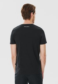 Czarna koszulka z krótkim rękawem z bawełny, z okrągłym dekoltem i białym logo nadrukowanym z tyłu w pobliżu dekoltu.