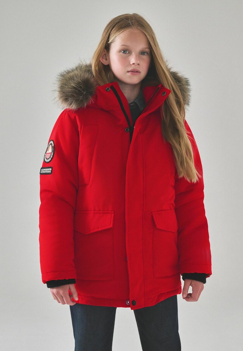Röd isolerad parkas med fickludd i huvan, två framfickor och ett svart innerfoder. Har logotypmärken på ärmen.