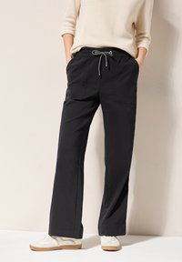 Black wide-leg pants with elastic waistband and drawstring. Two side pockets. Paired with light-colored sneakers. Smooth texture.
