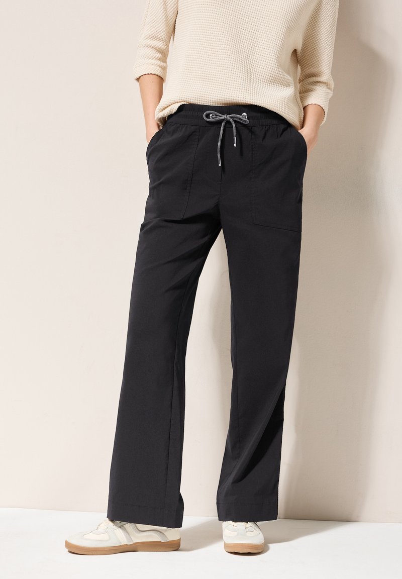 Black wide-leg pants with elastic waistband and drawstring. Two side pockets. Paired with light-colored sneakers. Smooth texture.