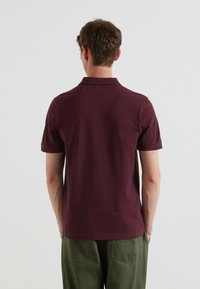 Burgundowa koszulka polo z krótkim rękawem, z płaskim kołnierzykiem, dopasowanym krojem i gładką fakturą, w połączeniu z zielonymi spodniami o szerokich nogawkach.