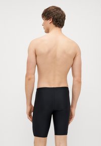 Calções de banho pretos feitos de um tecido liso e elástico, com um comprimento até à metade da coxa e uma cintura sem costuras para um ajuste confortável.