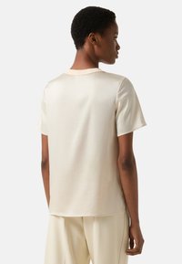 Top met korte mouwen in crèmekleurige, gladde stof met subtiele glans. Heeft een ronde halslijn en een losse pasvorm, gecombineerd met lichtgekleurde broek.