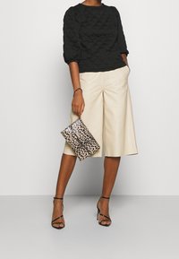 Svart vadderad topp med puffärmar, krämfärgade vida shorts, svarta sandaletter med remmar och en clutchtväck i leopardmönster. Släta material och modern design.