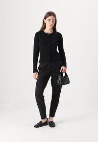 Cardigan nero con bottoni, pantaloni neri aderenti, mocassini neri e una piccola borsa nera. Texture liscia, design minimalista, colori monocromatici.