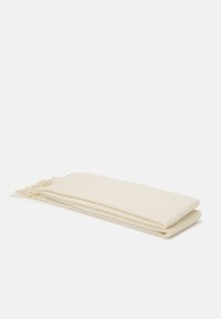 Pătură tricotată de culoare crem, cu o textură ribbed și capete franjurate, pliată ordonat în formă rectangulară.