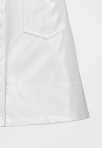 Bela krznena usnjena krilo z bleščečim zaključkom, z notranjim žepom spredaj, zapiranjem na gumbe in razširjenim robom. Gladek tekstura in čist dizajn.