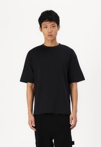 Must musta T-särk ümmarguse kaeluse, lühikeste varrukate, ja vabalt langeva lõikega, millel on minimalistlik disain. Ei ole nähtavaid mustreid ega logo.