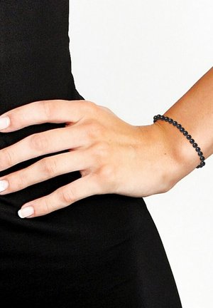 Bracelet élastique noir avec des perles rondes lisses, présentant un design simple et une texture uniforme, porté sur une main contre un fond noir.