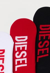Baumwollsocken in Weiß, Rot und Schwarz. Jede trägt das Wort "DIESEL" in kontrastierenden Farben. Glatte Textur, abgerundete Bündchen.