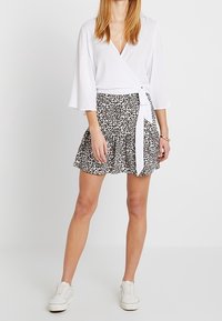 Top blanco con mangas anchas, combinado con una falda de estampado de leopardo en blanco y negro que presenta un diseño acampanado y una cintura atada. Zapatillas blancas.