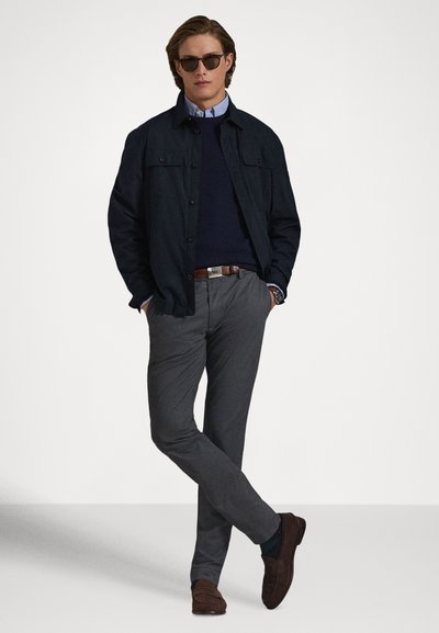 Laza öltözék sötét farmerdzsekivel, tengerkék pulóverrel, világoskék inggel, szürke nadrággal és barna velúr mokaszinokkal. Napszemüveg is tartozik hozzá.