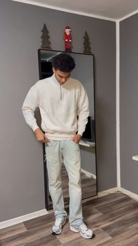 Sweatshirt cinza claro com fecho quarter-zip e punhos canelados, combinado com calças de ganga azul claro desgastadas e sapatilhas desportivas cinzentas. Fundo com espelho refletor.